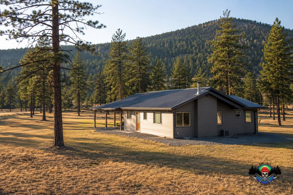 A rural BC interior home with gravel against the foundation and conifers thinned well back from the walls